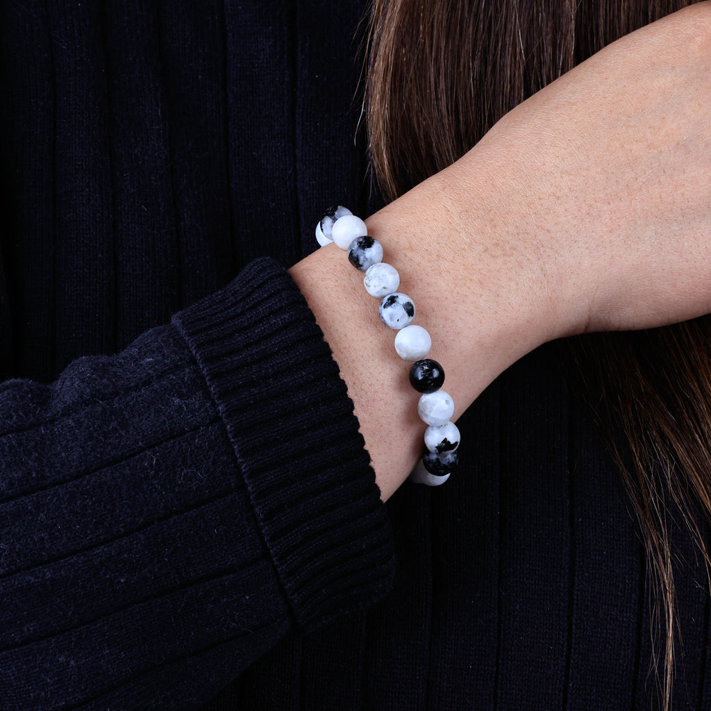 Person wearing a black and white beaded bracelet on a dark shirt and showing discrete pill holder