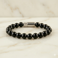 Black beaded bracelet with a silver clasp on a marble surface