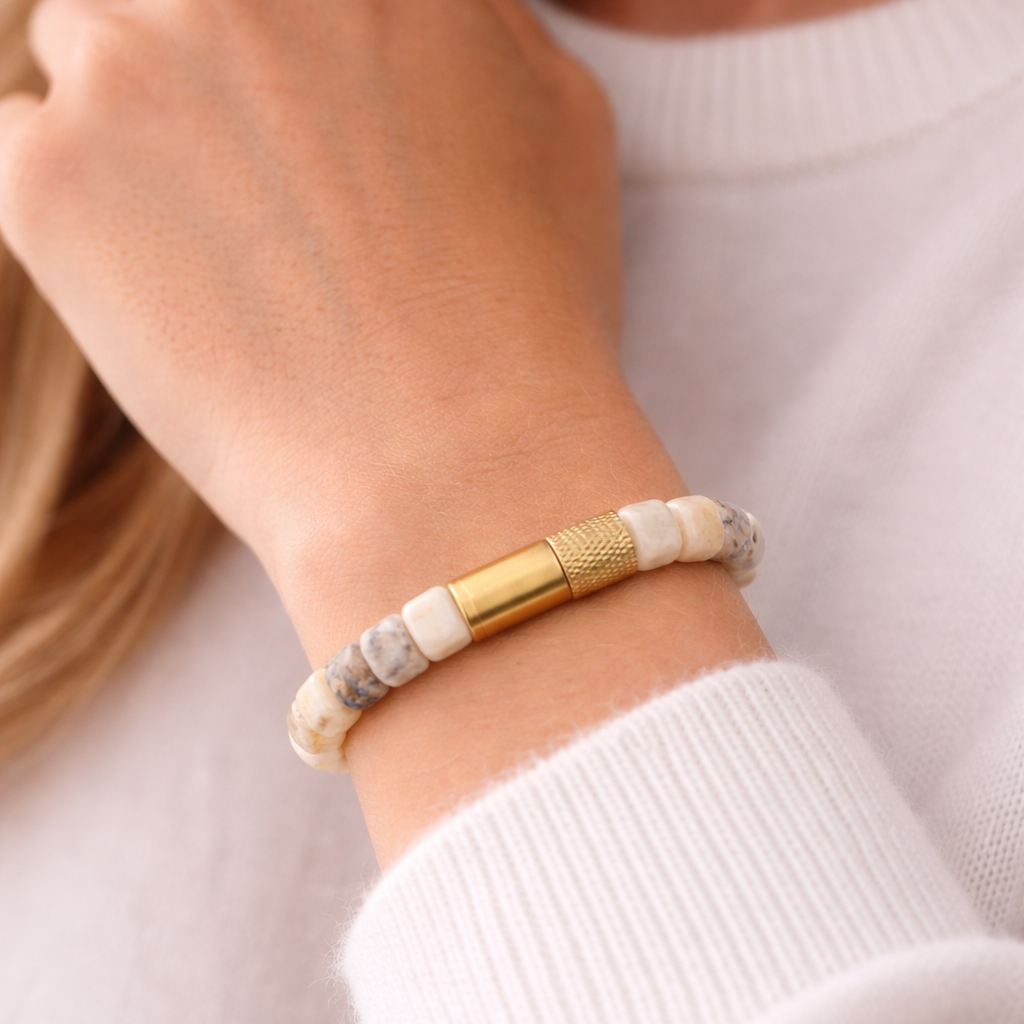 Close-up of a hand wearing a gold and beige bracelet on a blurred background