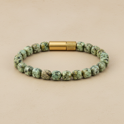 A beaded bracelet made of rounded, polished turquoise-green and brown stone beads with a textured gold-tone metal clasp, displayed on a dark slate surface.