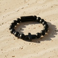 Black beaded bracelet with a cross charm on a beige surface