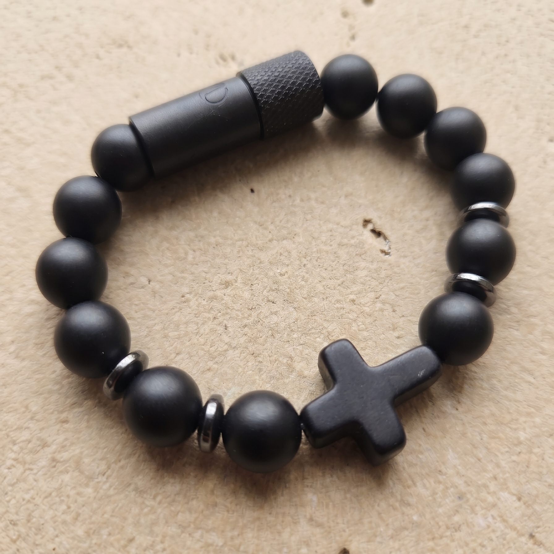 Black beaded bracelet with a cross charm on a beige surface