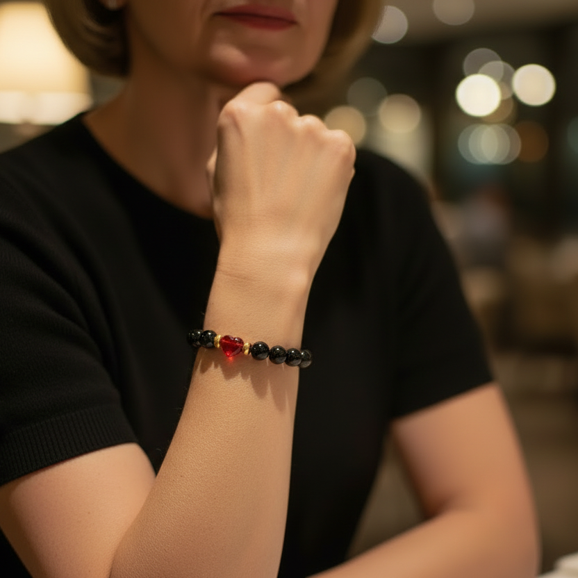 Black beaded bracelet with a red heart charm and gold accents on a white background