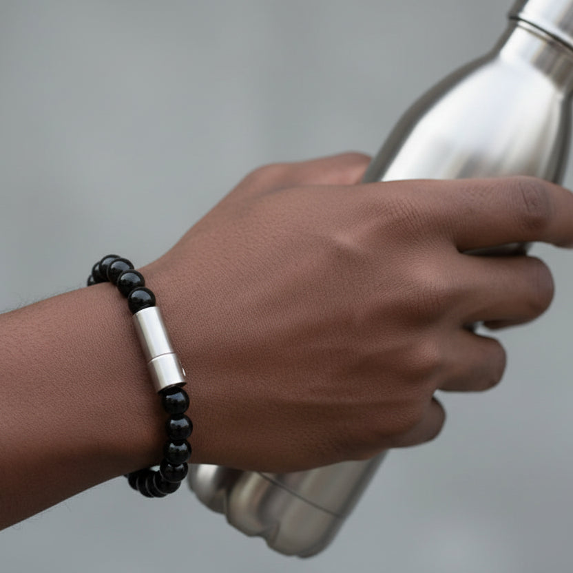 Black beaded bracelet with a silver vessel that is pill holder for medication on a white background