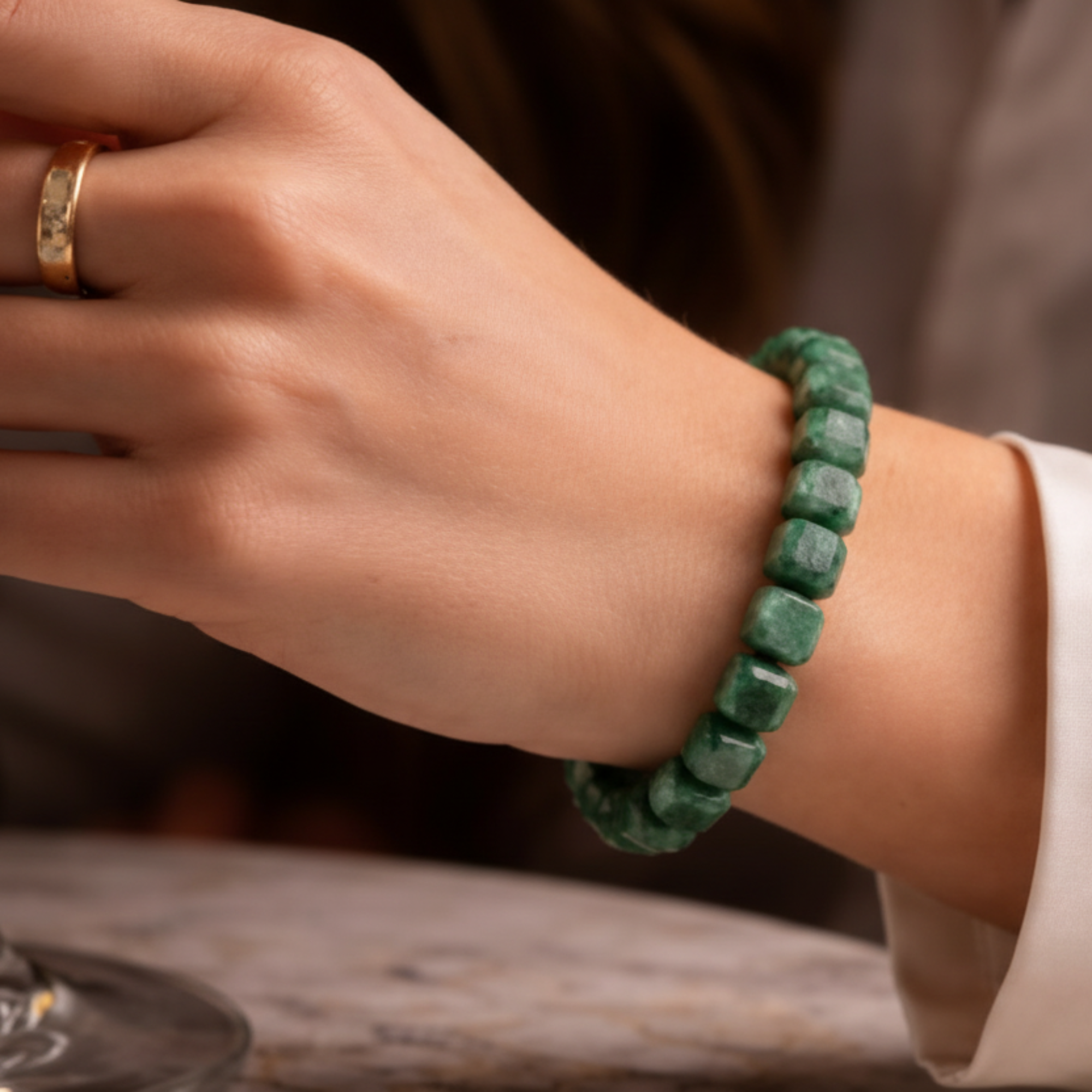 Person wearing a green beaded bracelet with a glass of wine in the background