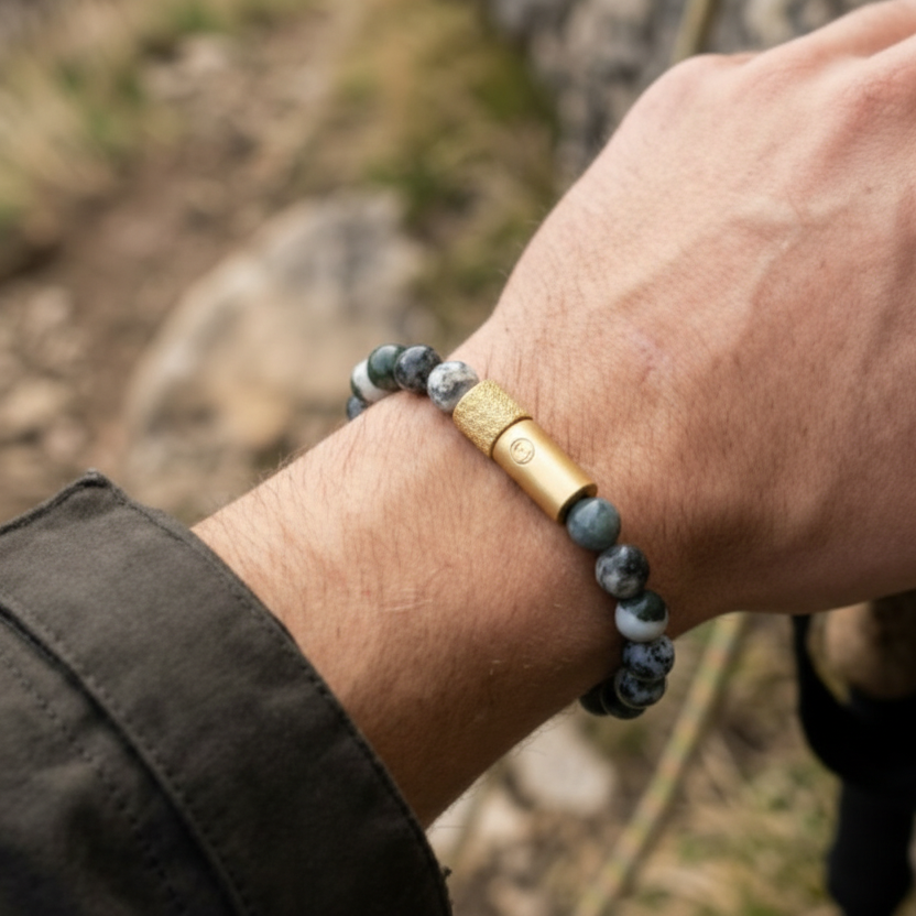 Hand wearing a bracelet with a natural stone and gold bar design, against a rocky background. discrete pill holder