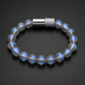A beaded bracelet made of translucent white beads with a blue iridescent sheen, featuring a silver-toned cylindrical clasp with a textured knurled band, set against a dark gray background.